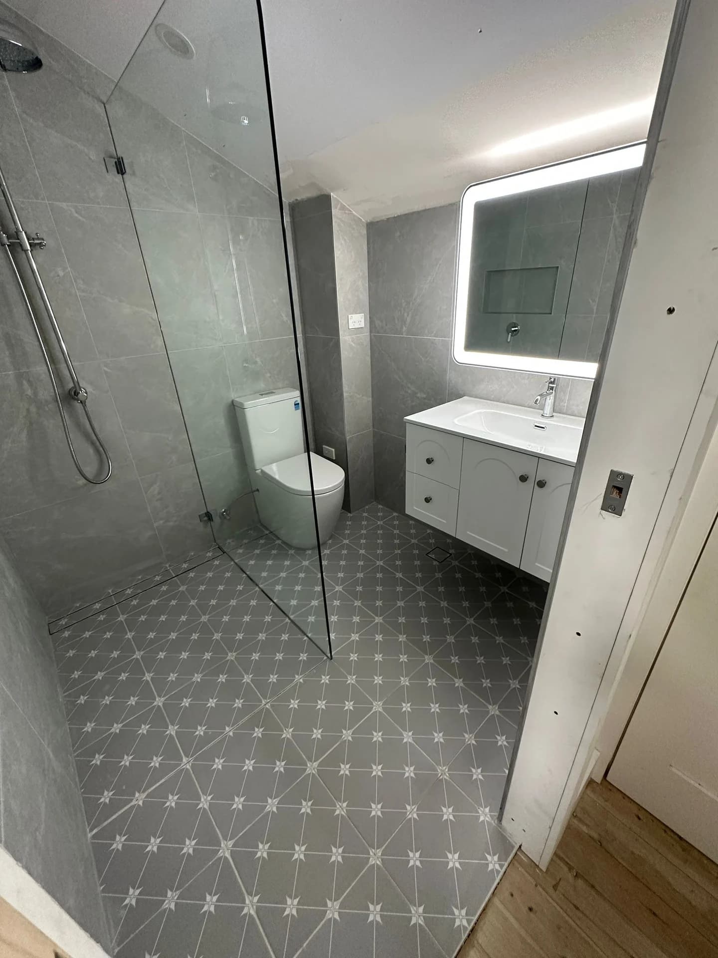 Grey bathroom wall tiles and patterned floor beside a white vanity