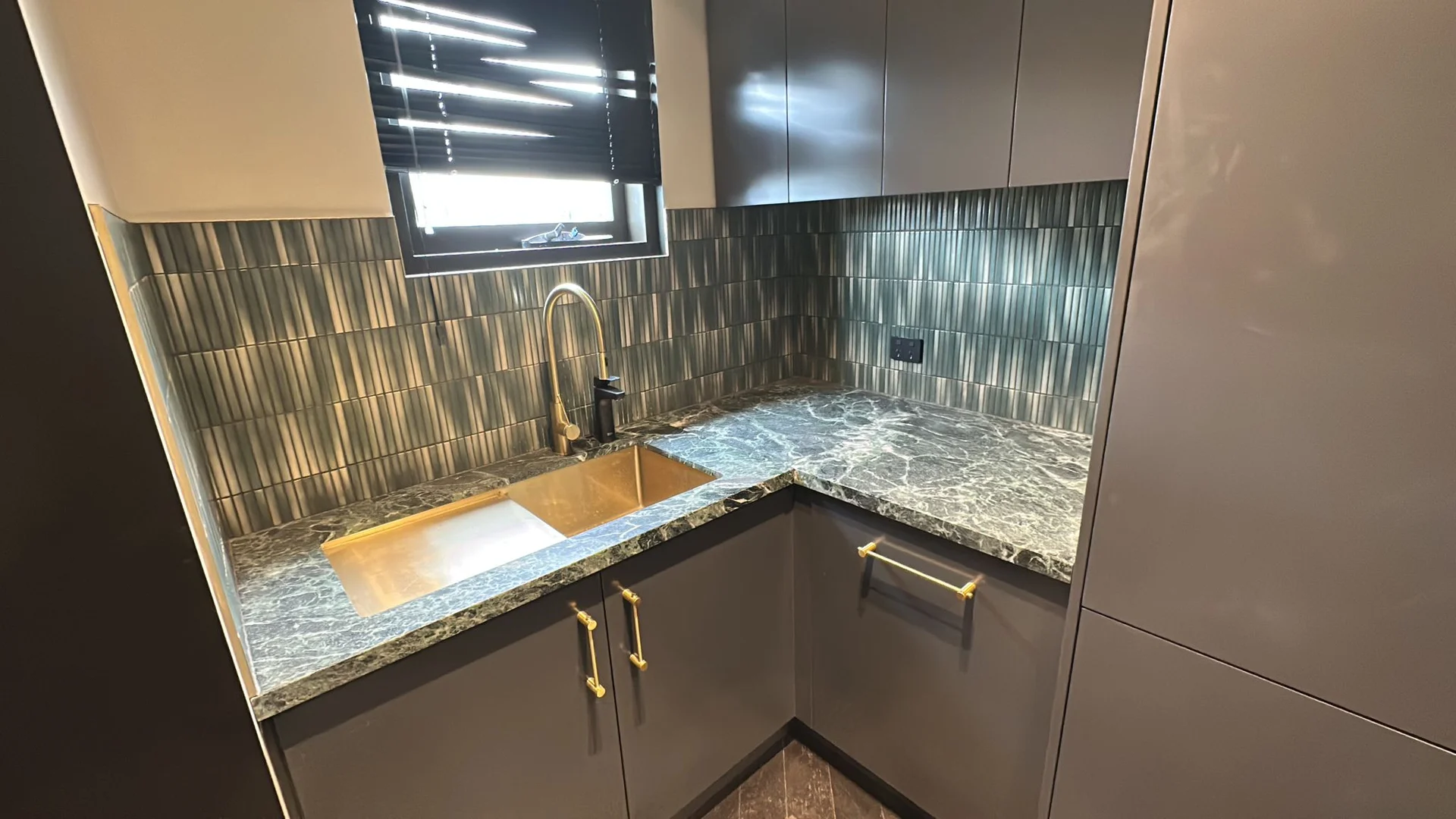 Green splashback tiles beneath a kitchen window