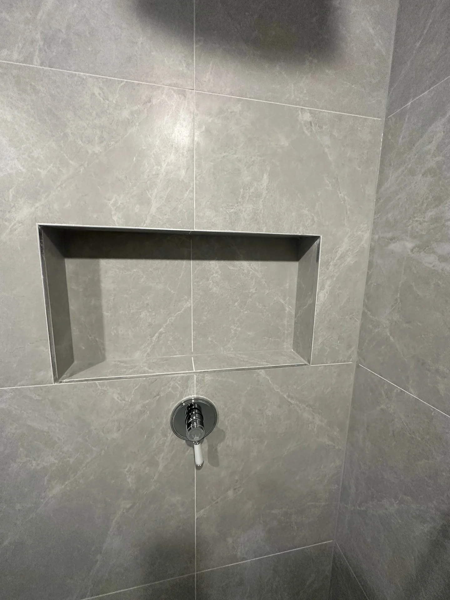 A recessed shower niche within grey wall tiles