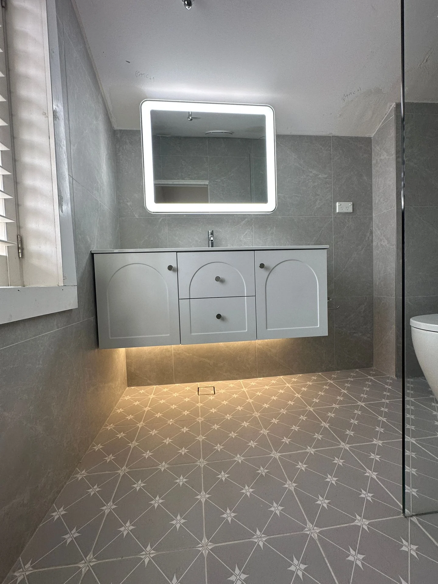 Grey bathroom wall tiles above a patterned floor