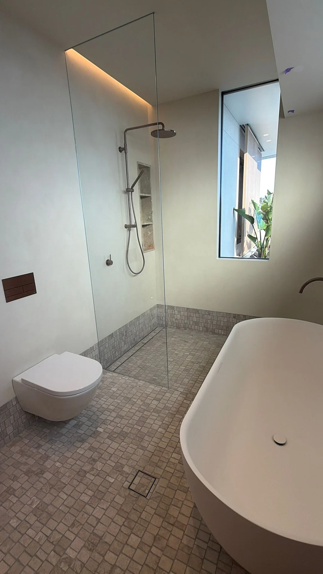 Mosaic bathroom floor beside a bath and wall-hung toilet