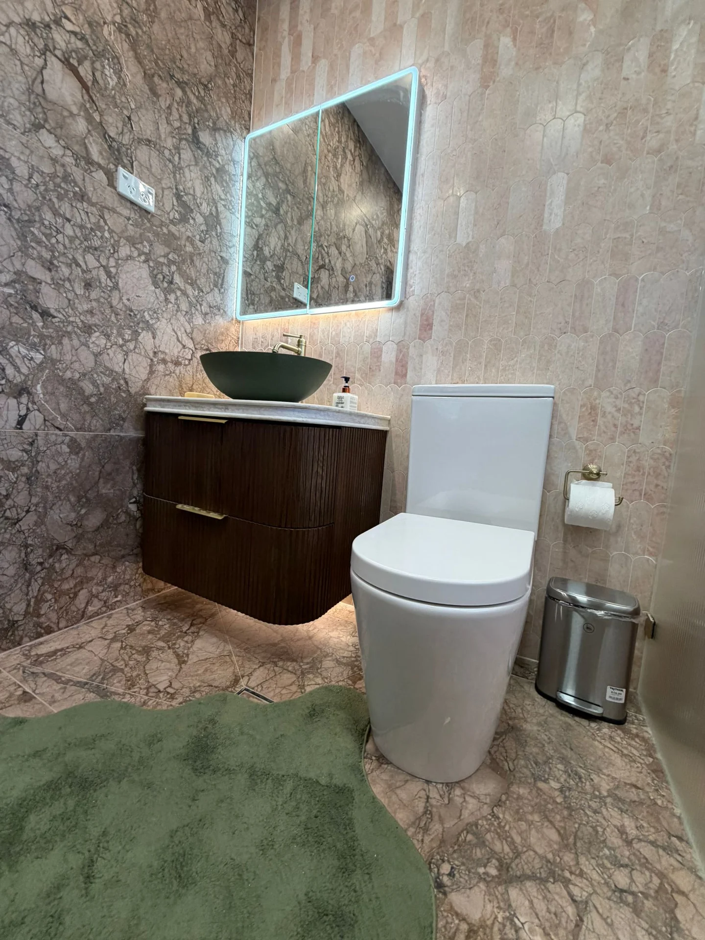 Pink stone-look wall and floor tiles around a bathroom vanity and toilet