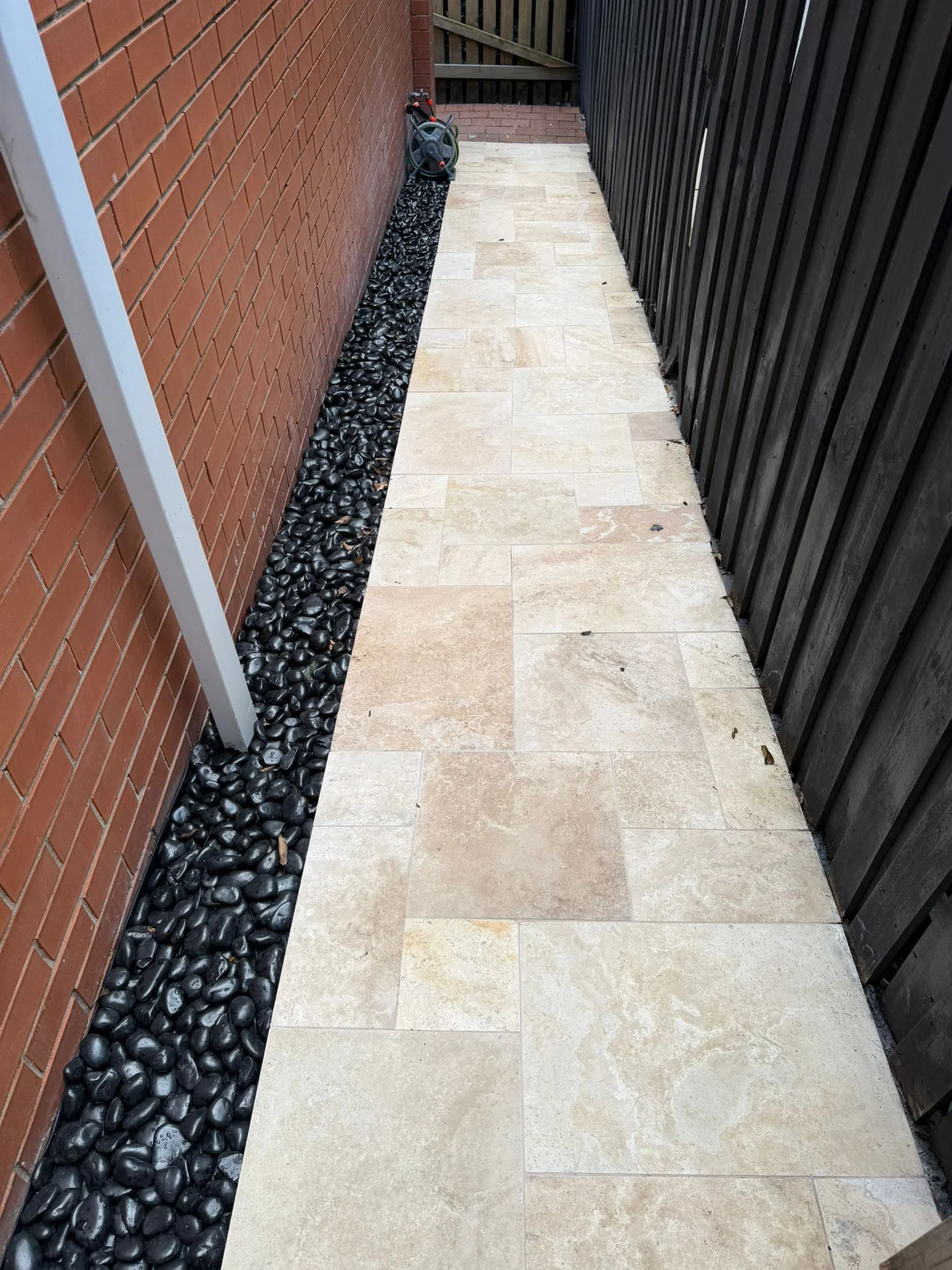 Pale tiles along a side path beside black pebbles