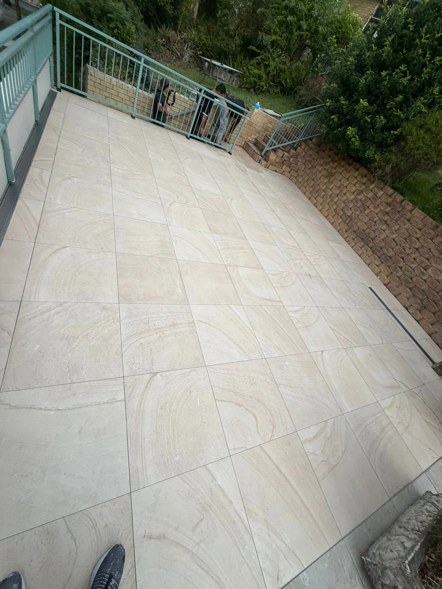 Pale outdoor tiles across a landing beside green railings