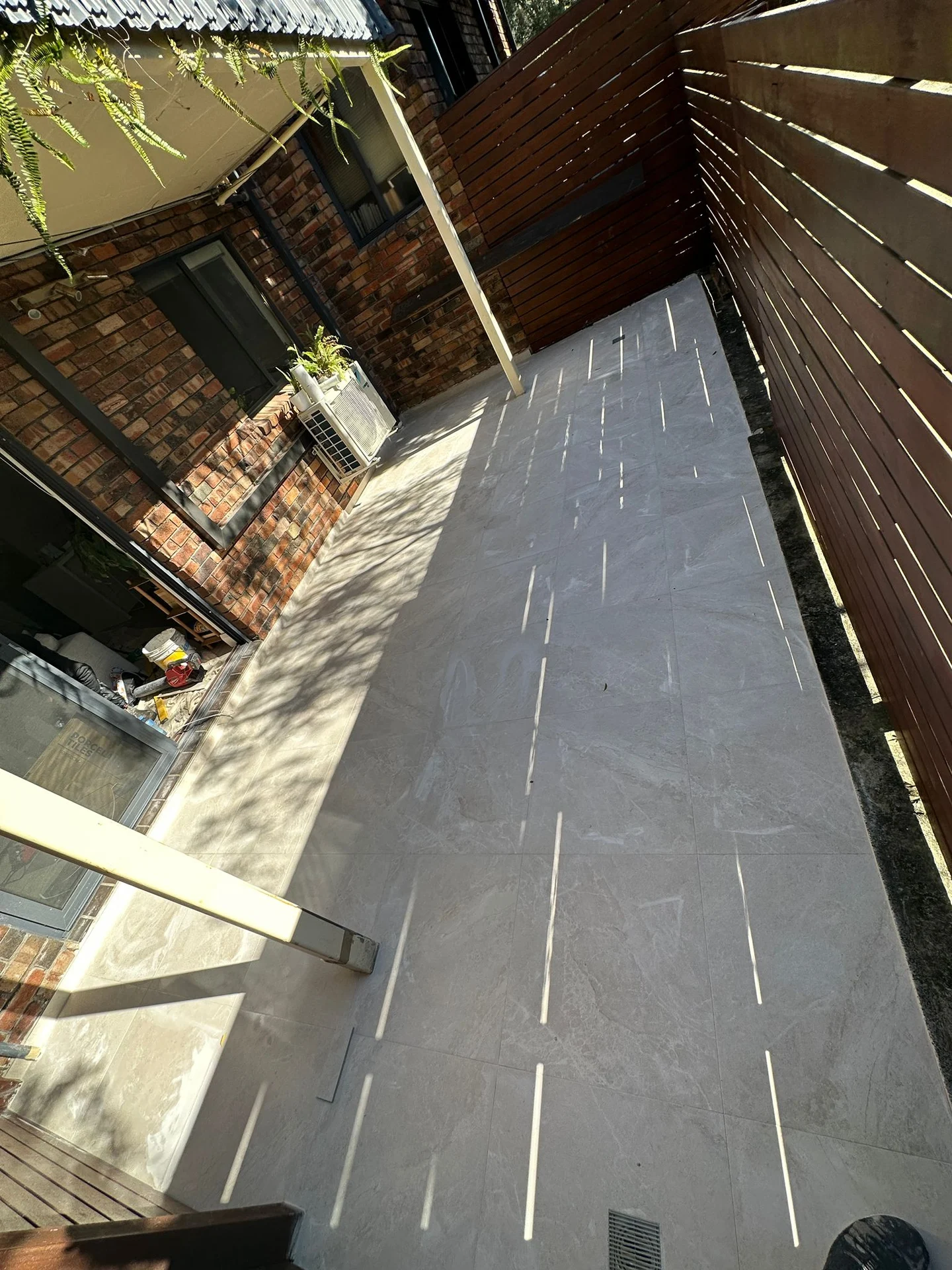 Grey floor tiles across a courtyard beside timber fencing